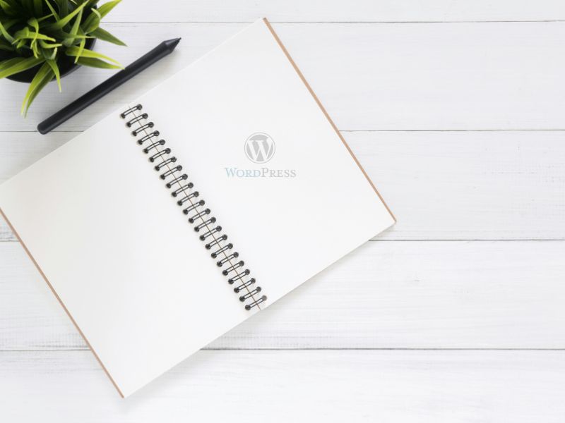 blogger writing content on notebook beside laptop